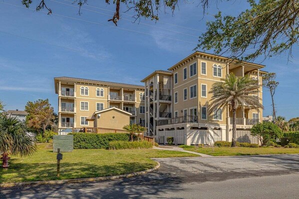 A multi-story residential building with balconies, a covered front porch, and a well-maintained lawn.