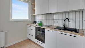 Une cuisine moderne avec des meubles blancs, un évier noir et une fenêtre donnant sur un ciel dégagé.