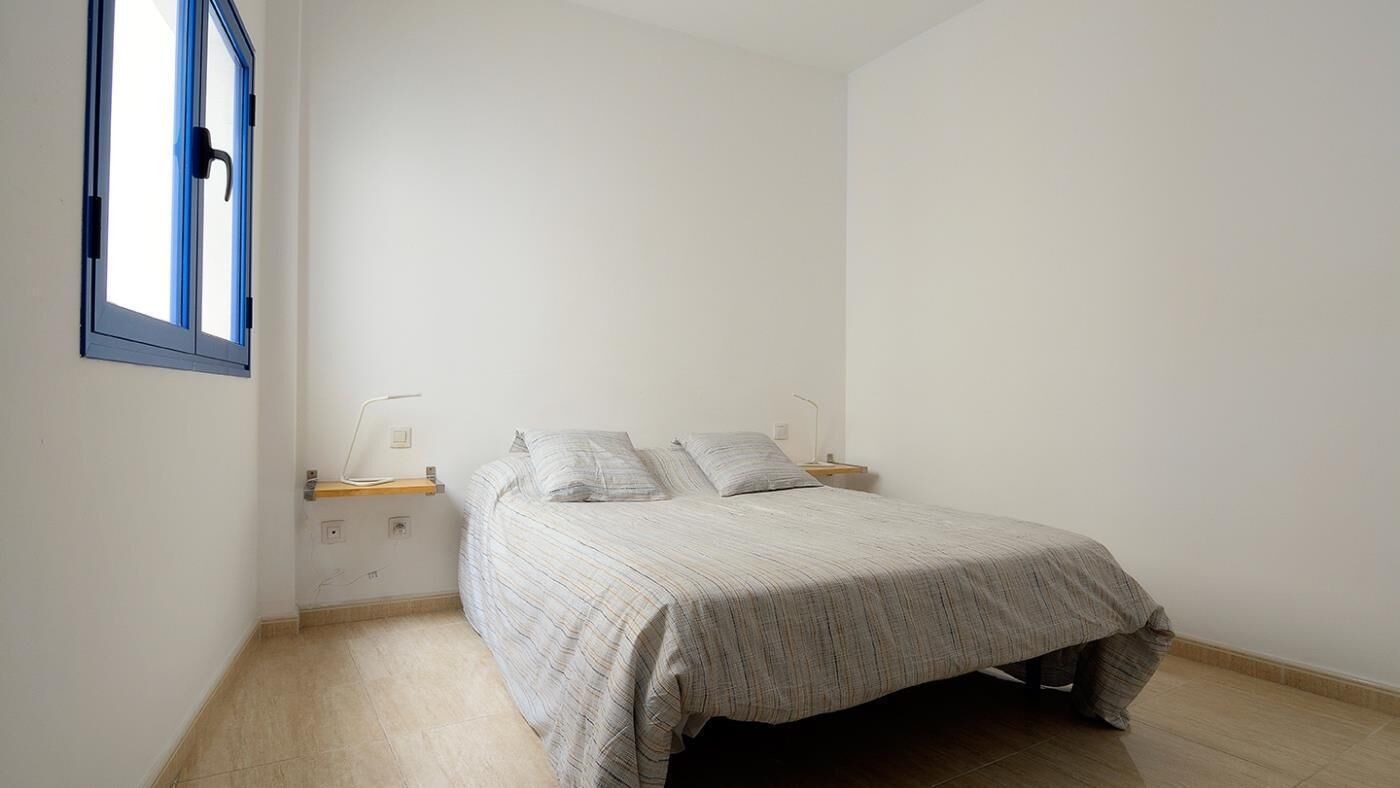 A bedroom with a bed, a nightstand, a lamp, and a window with blinds.