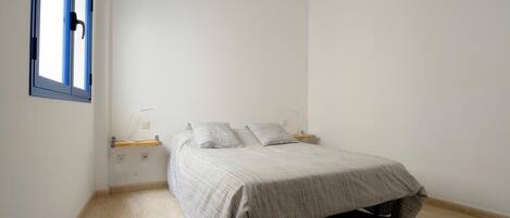 A bedroom with a bed, a nightstand, a lamp, and a window with blinds.
