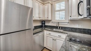 Eine Küche mit weißen Schränken, einem Edelstahlkühlschrank, einem eingebauten Backofen und einer Arbeitsplatte aus Granit.