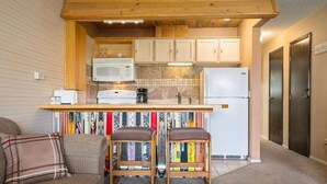 A compact kitchen with wooden cabinets, a microwave, a refrigerator, and a coffee maker. There are two bar stools with books on the counter.