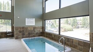A spa room with a large window, a hot tub, and a chair.