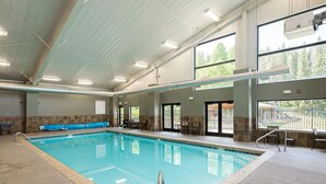 An indoor swimming pool with clear water, surrounded by tiled walls and a high ceiling with fluorescent lighting.