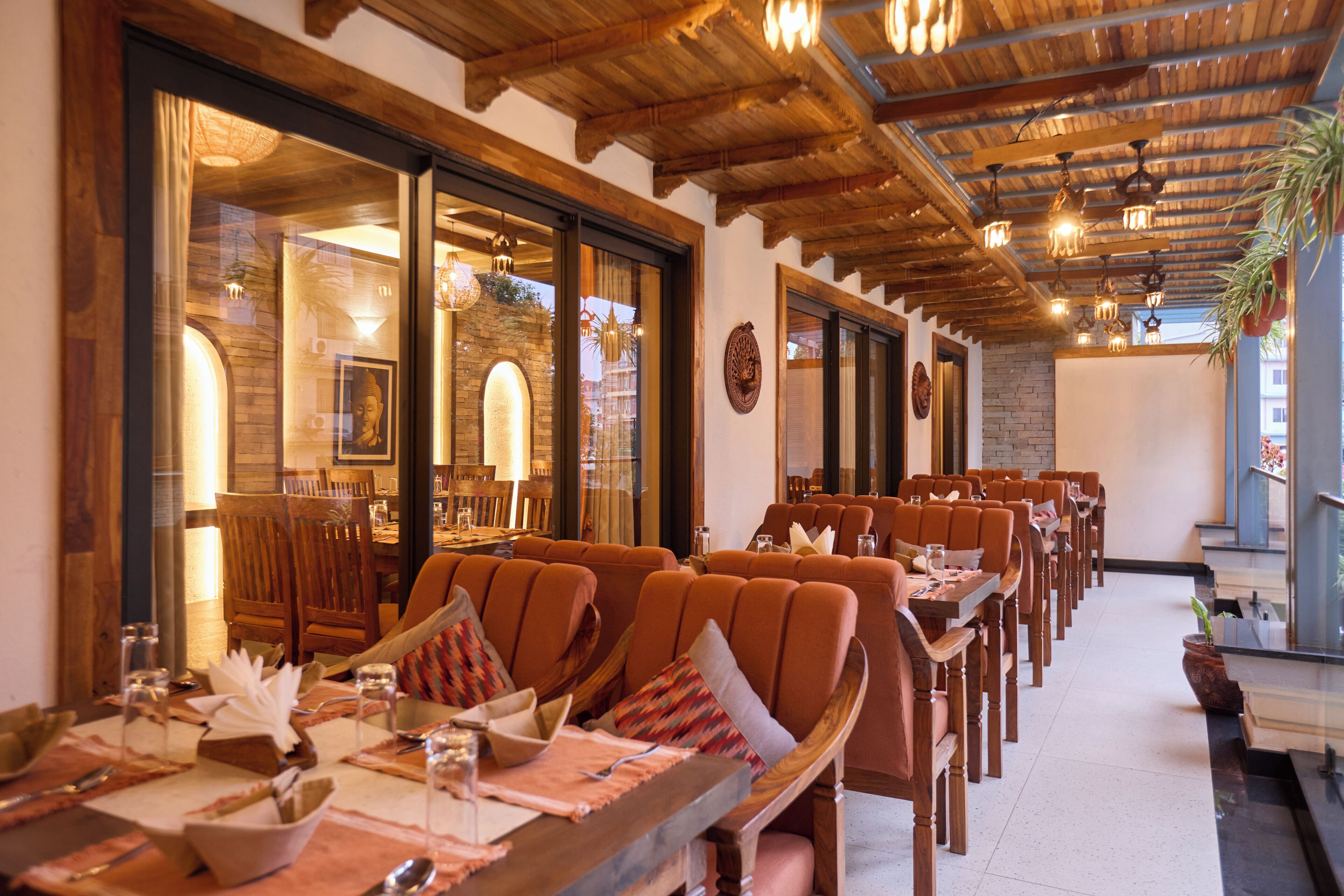 A restaurant with wooden tables and chairs, large windows, and a stone wall.