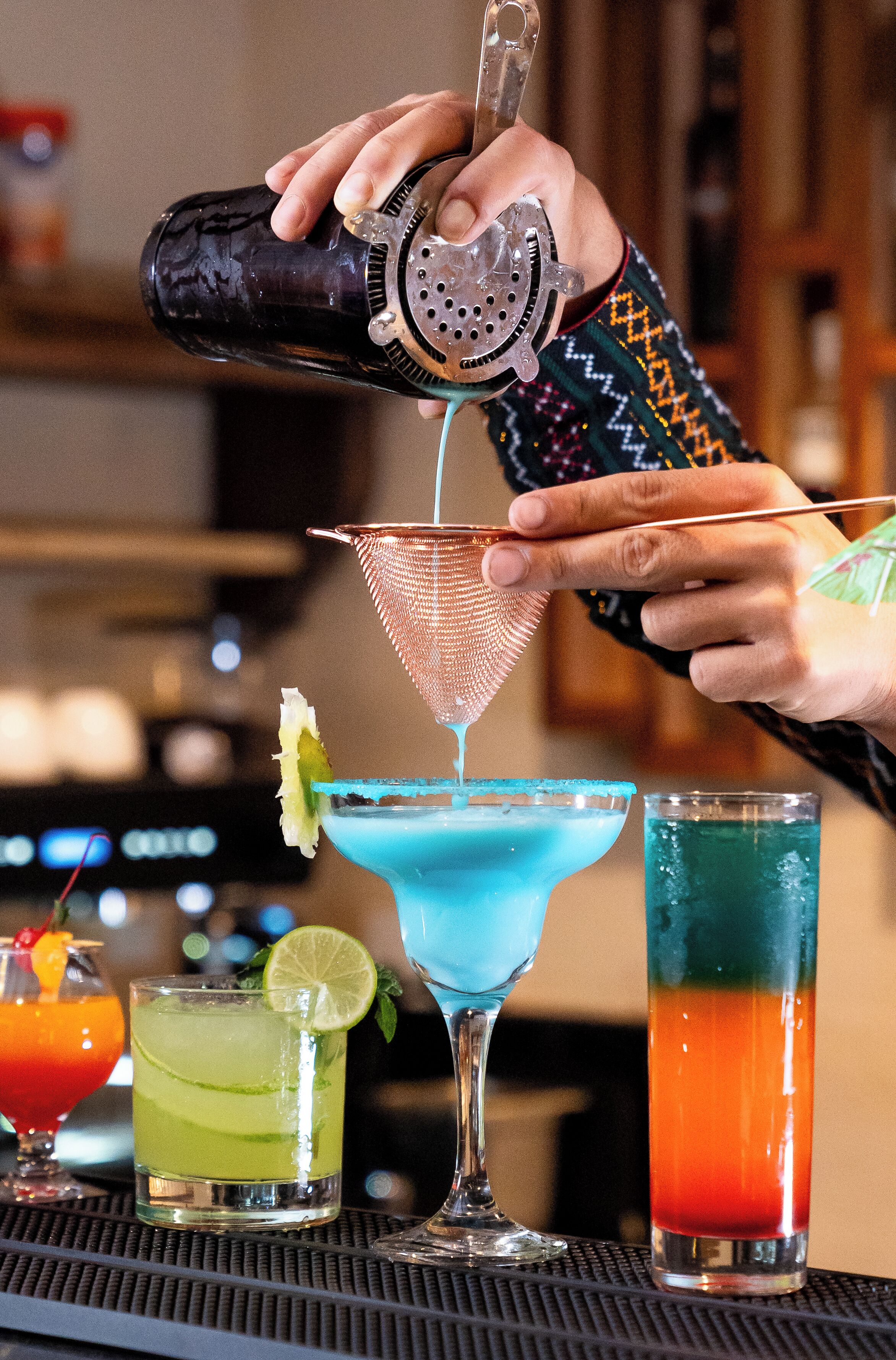 Un bartender sirviendo una bebida en un vaso de cóctel azul.