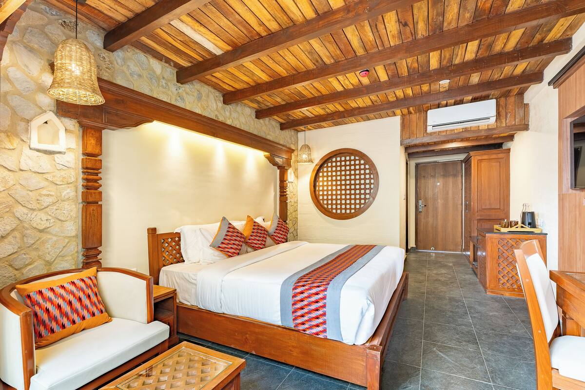 A spacious bedroom with a large bed, wooden furniture, stone walls, and a wooden ceiling.