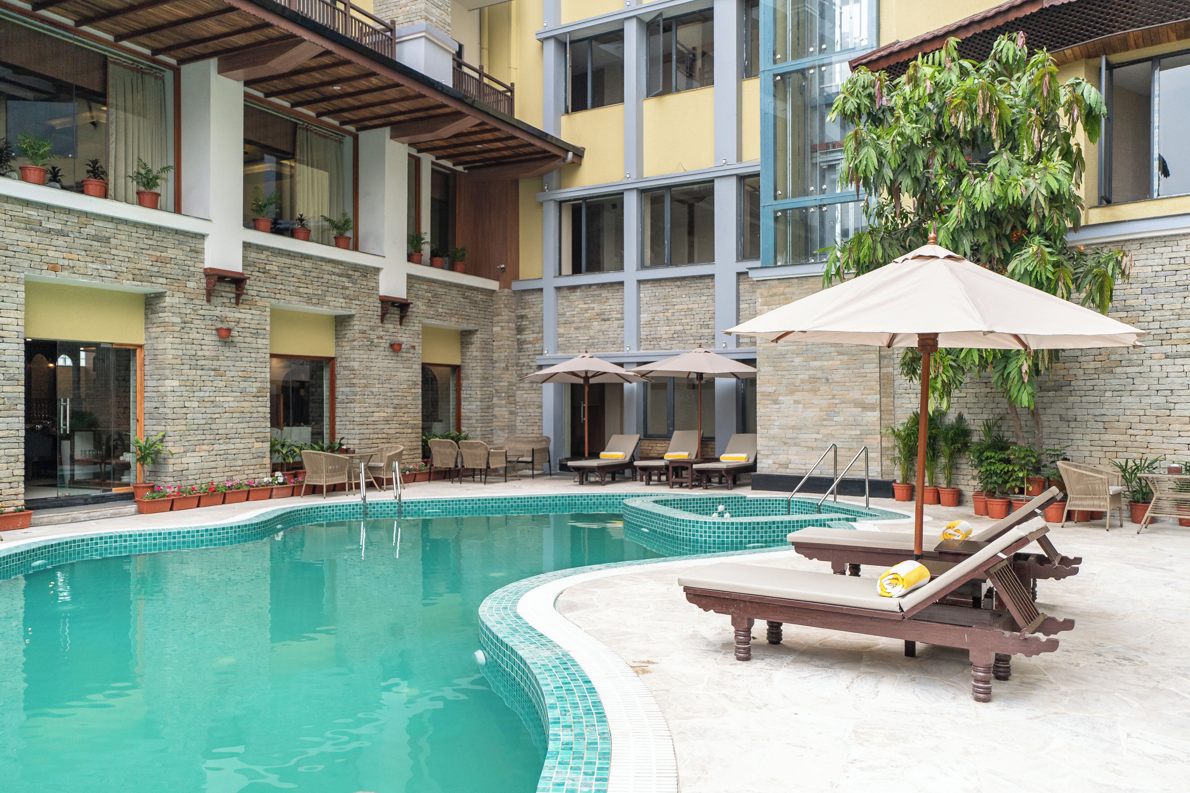 A pool area with lounge chairs and umbrellas, surrounded by potted plants and a stone building.