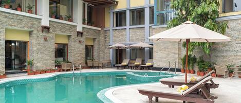 A pool area with lounge chairs and umbrellas, surrounded by potted plants and a stone building.