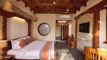 Ein Hotelzimmer mit Holzbalkendecke, einem Bett mit weißer Bettwäsche, einer runden Wanddekoration, einem an einer Ziegelwand montierten Fernseher und einem Holzstuhl.