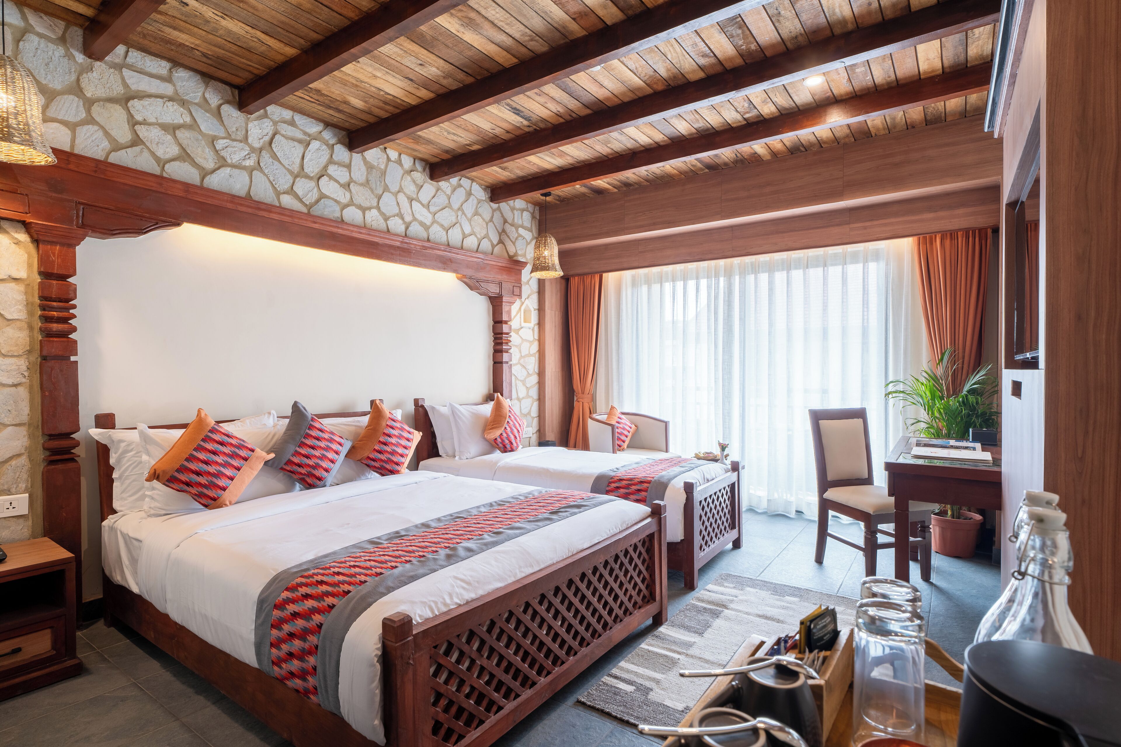 Habitación de hotel con dos camas, pared de piedra, vigas de madera, un escritorio y una planta en maceta.