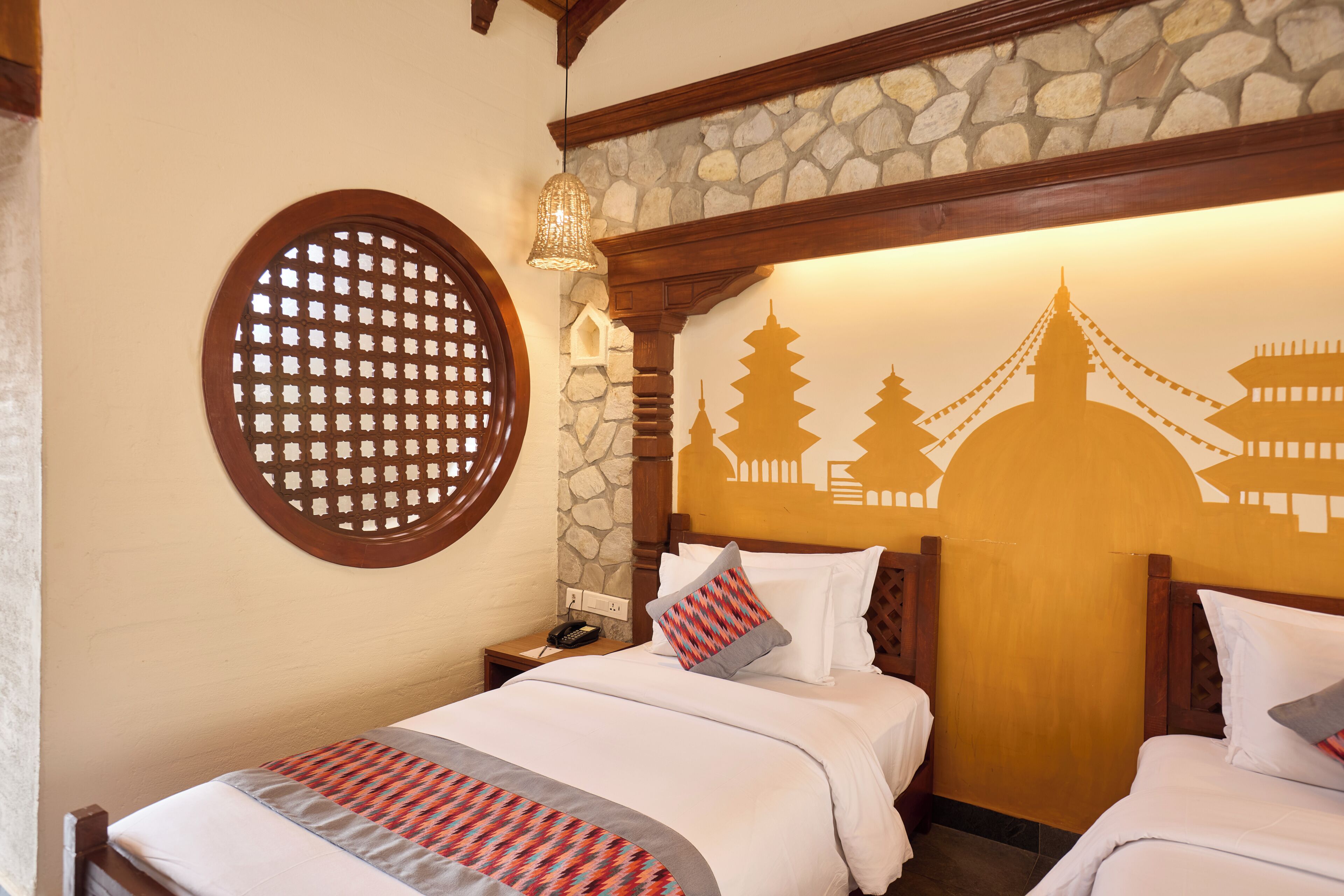 Ein Hotelzimmer mit zwei Betten, einer Steinsäule, einer dekorativen Holzbalkendecke und einem Wandgemälde.