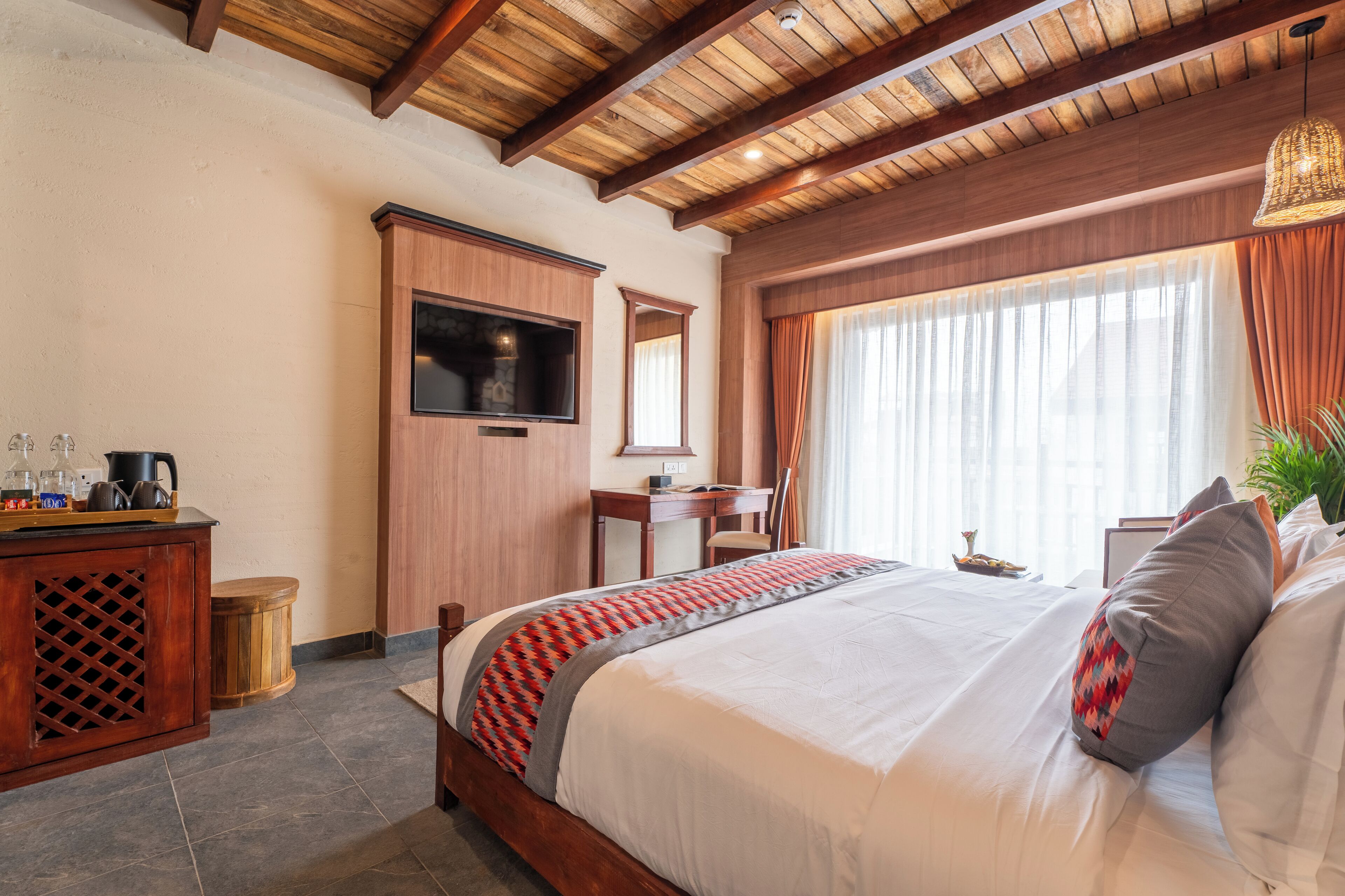 Habitación de hotel con techo de madera, una cama grande con ropa de cama estampada, un televisor montado en la pared y un escritorio con silla.