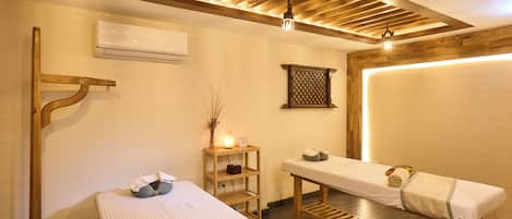 Un cuarto de spa con una cama, una camilla de masaje, un estante con toallas y un aire acondicionado de pared.