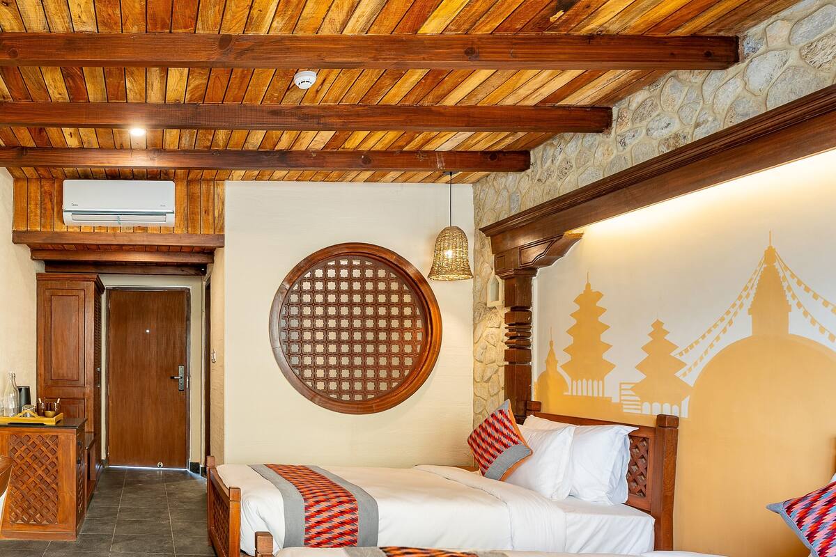 A hotel room with two beds, a wooden ceiling, a stone wall, and a decorative wall hanging.