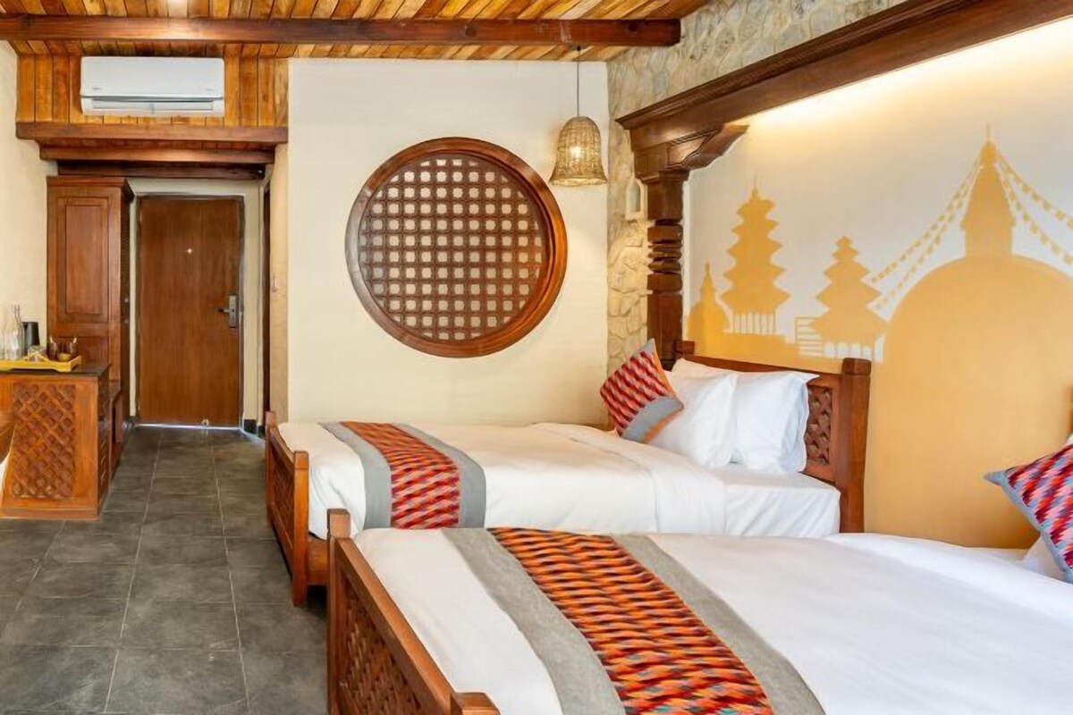 Quarto de hotel com duas camas, uma cabeceira de madeira, um painel redondo na parede e uma parede de pedra.