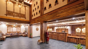 Un hall d’entrée spacieux comprenant un comptoir d’accueil, un espace salon et des éléments décoratifs tels que des poutres en bois et des motifs muraux traditionnels.