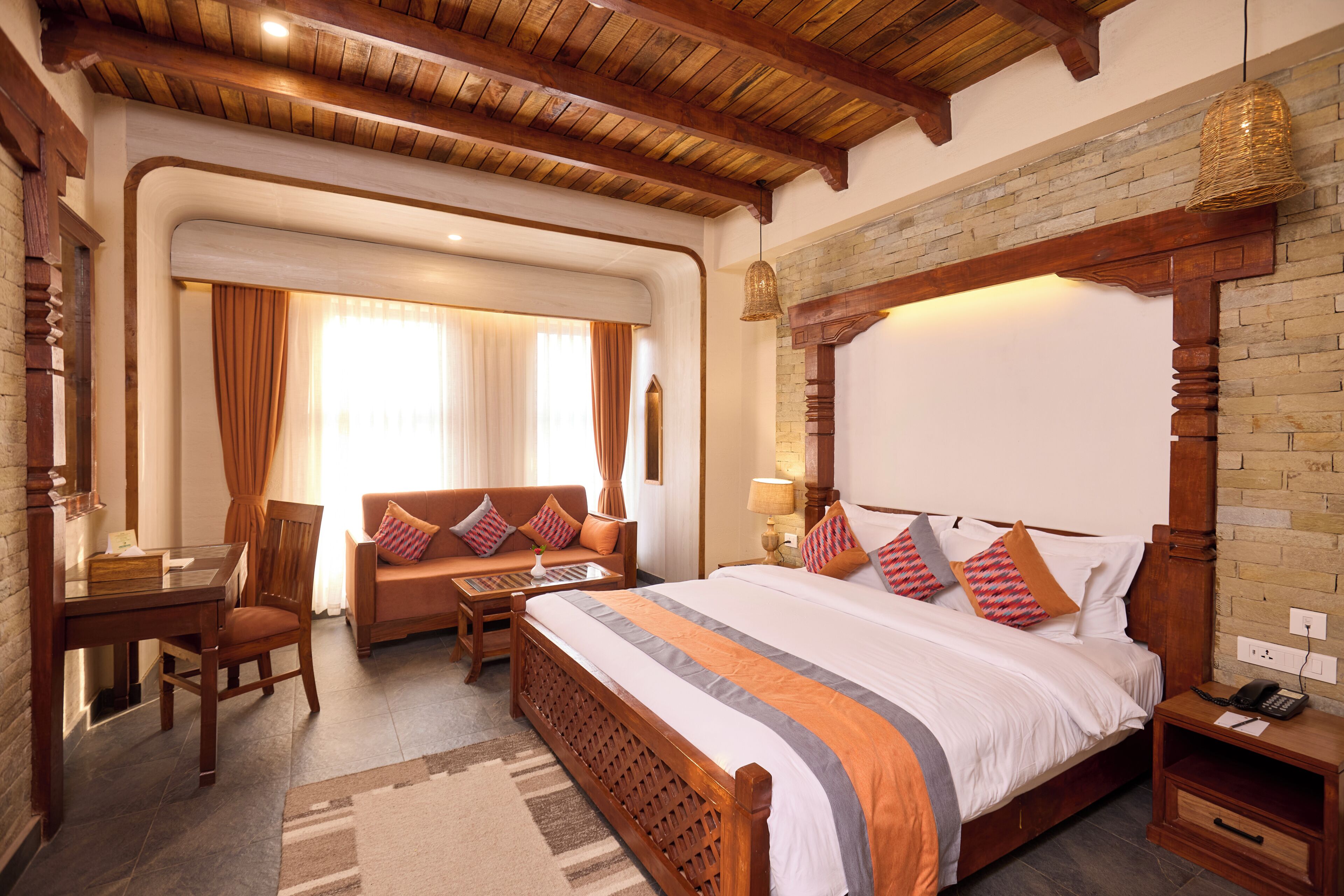 A hotel room with a large bed, a wooden headboard, a desk with a chair, a sofa, and a hanging light fixture.