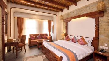 A hotel room with a large bed, a wooden headboard, a desk with a chair, a sofa, and a hanging light fixture.