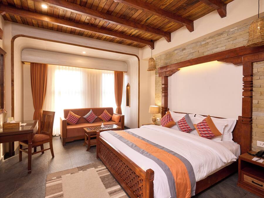 A hotel room with a large bed, a wooden headboard, a desk with a chair, a sofa, and a hanging light fixture.