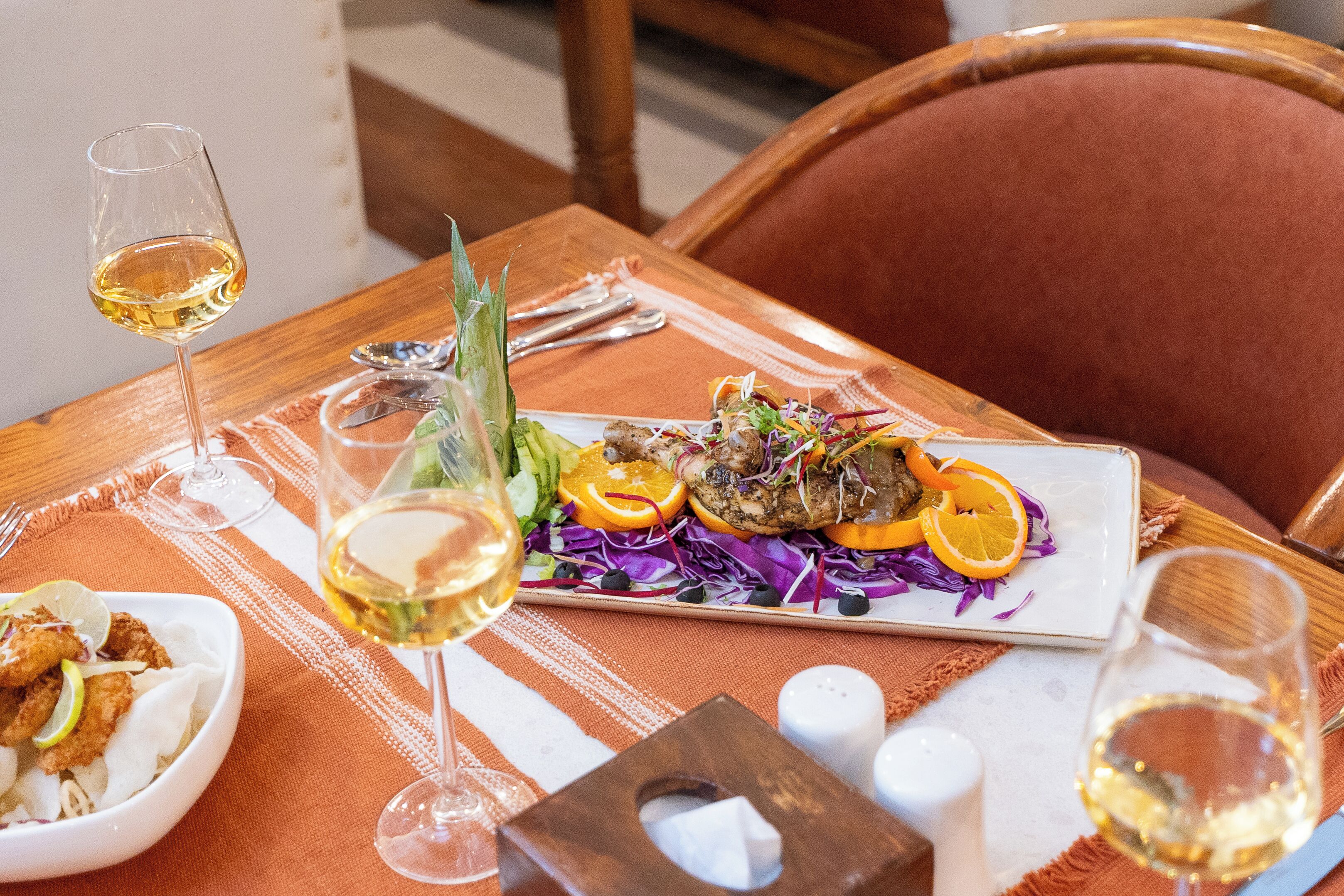 A dining table with a plate of food, two glasses of white wine, and a salt and pepper shaker.