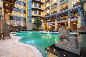 Un hotel de varios niveles con piscina, asientos al aire libre y una estatua de león de piedra.