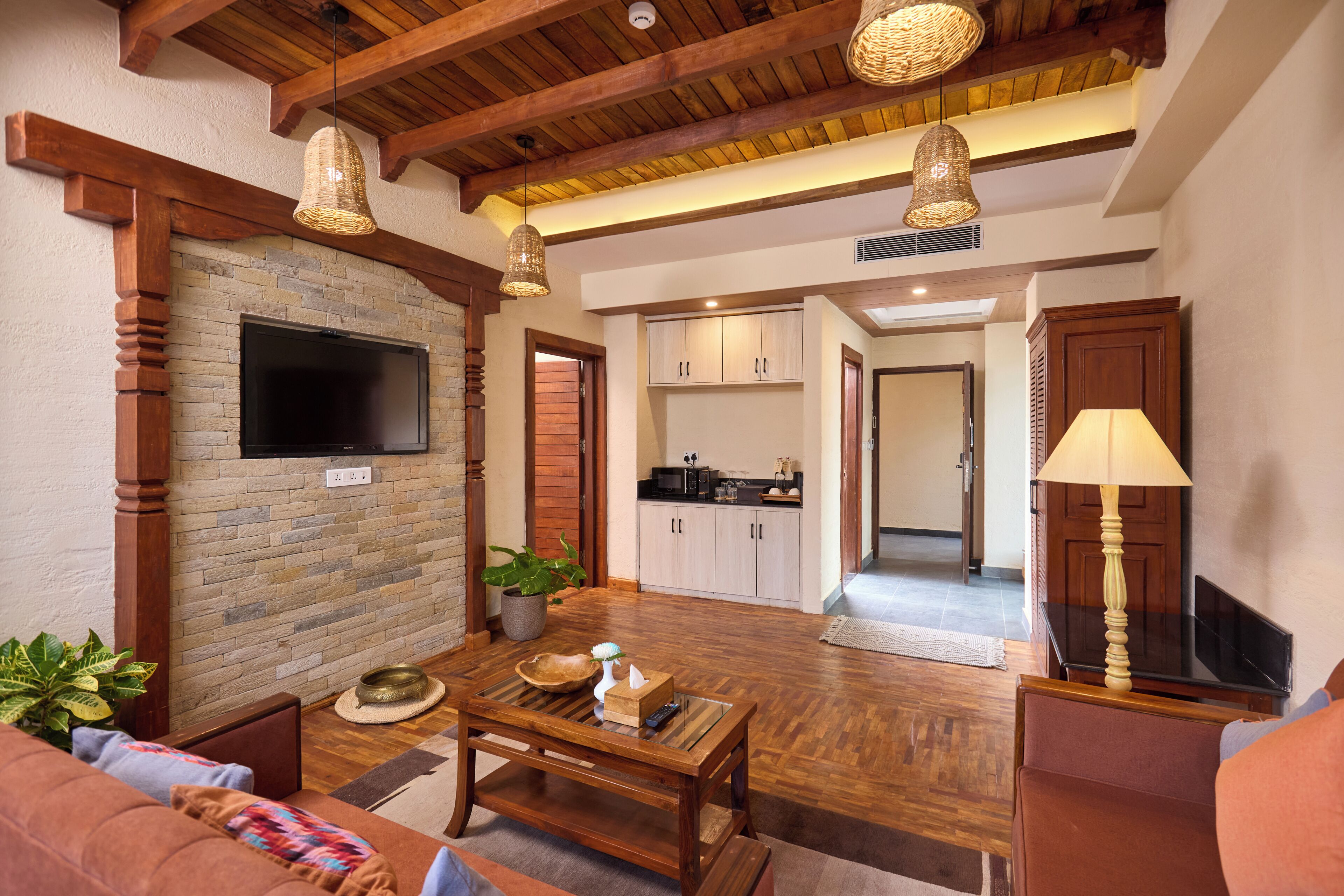 A living room with a TV, wooden furniture, a kitchen in the background, and a staircase leading to another level.