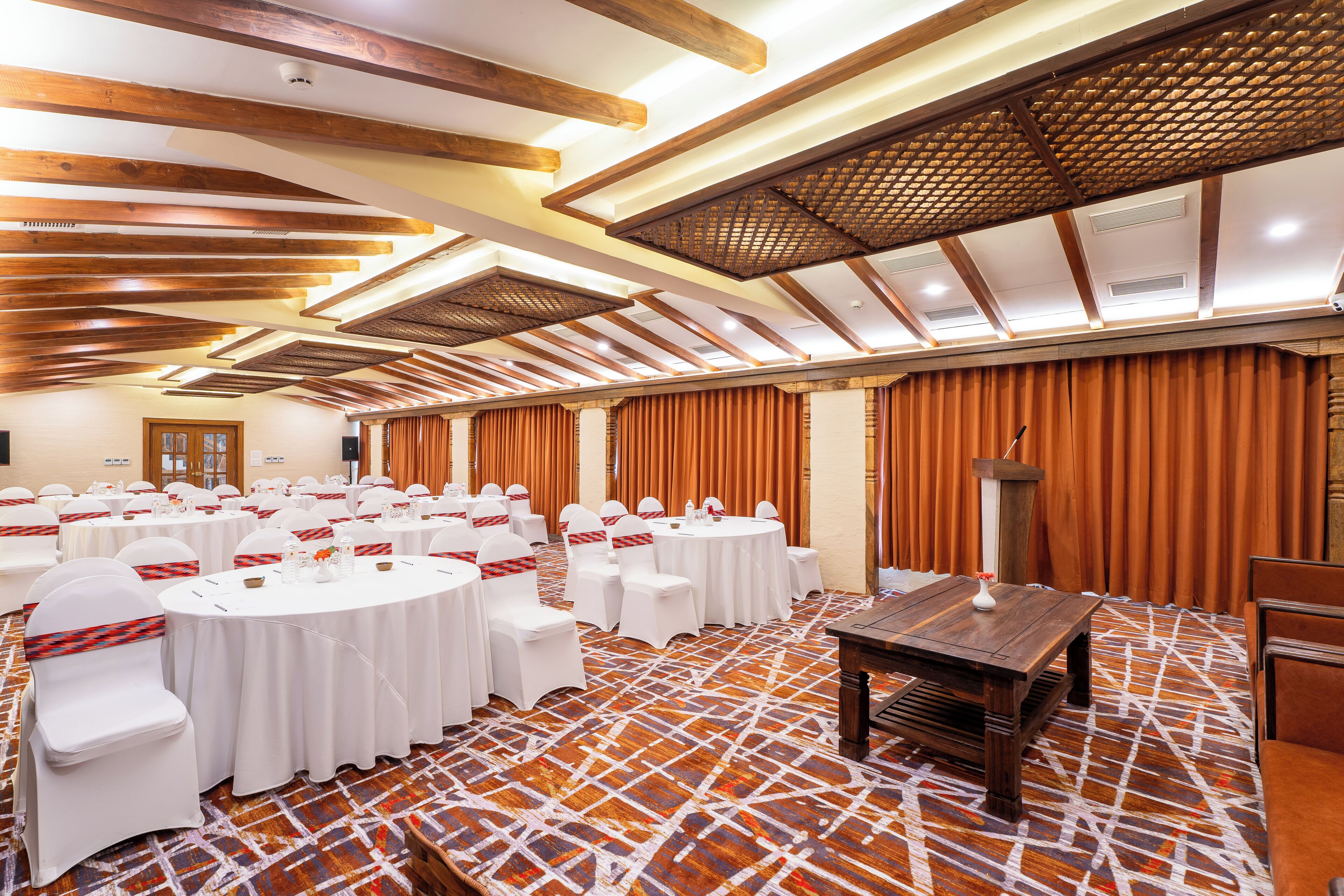Une salle de conférence avec des tables rondes, des chaises blanches et un tapis à motifs.