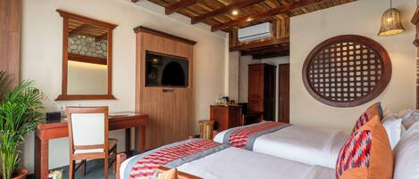 Una habitación de hotel con dos camas, un escritorio con silla, televisión y una planta en maceta.