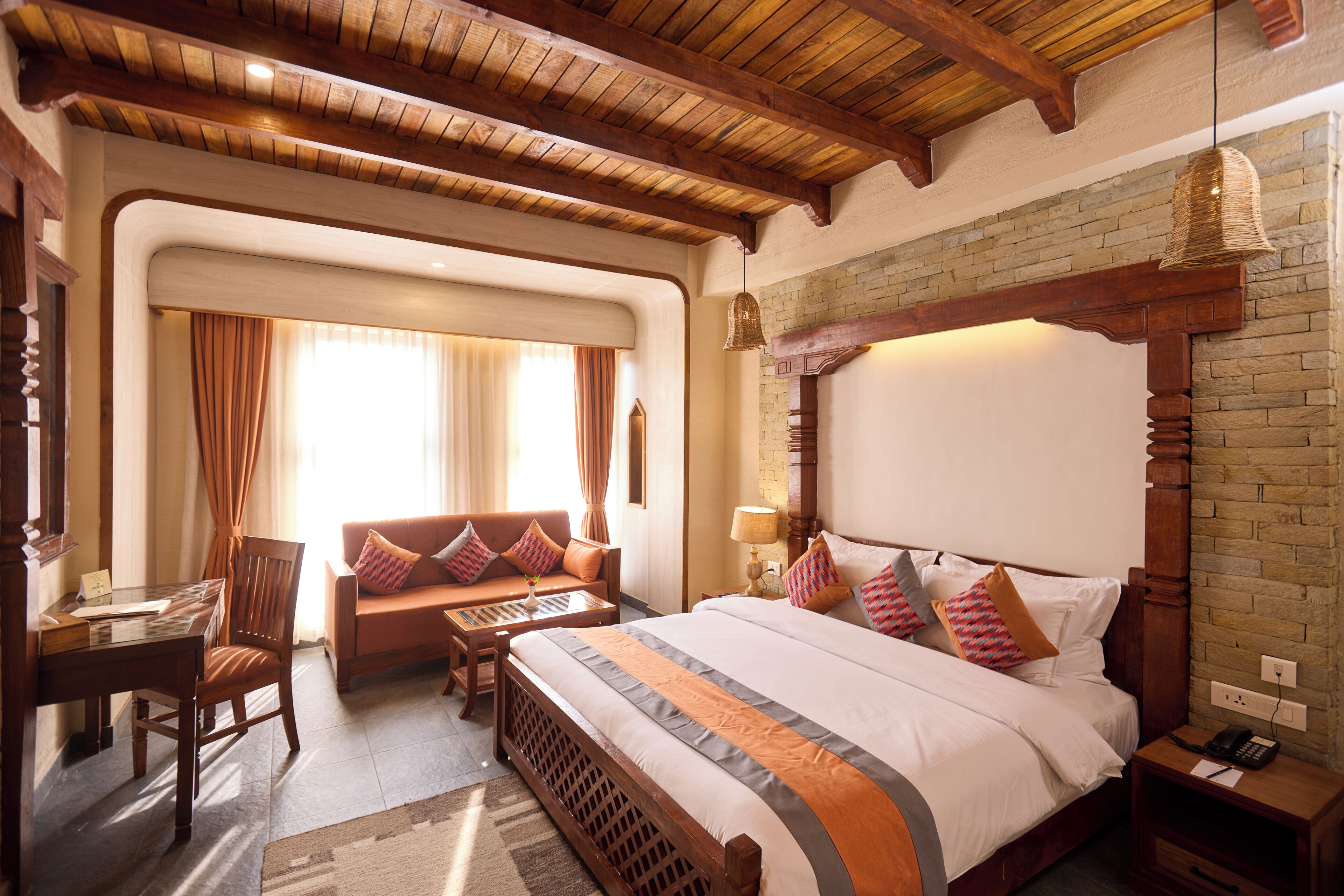 A hotel room with a large bed, a wooden headboard, a desk, and a sofa.