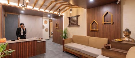 A reception area with a wooden reception desk, a sofa, and a Buddha statue.