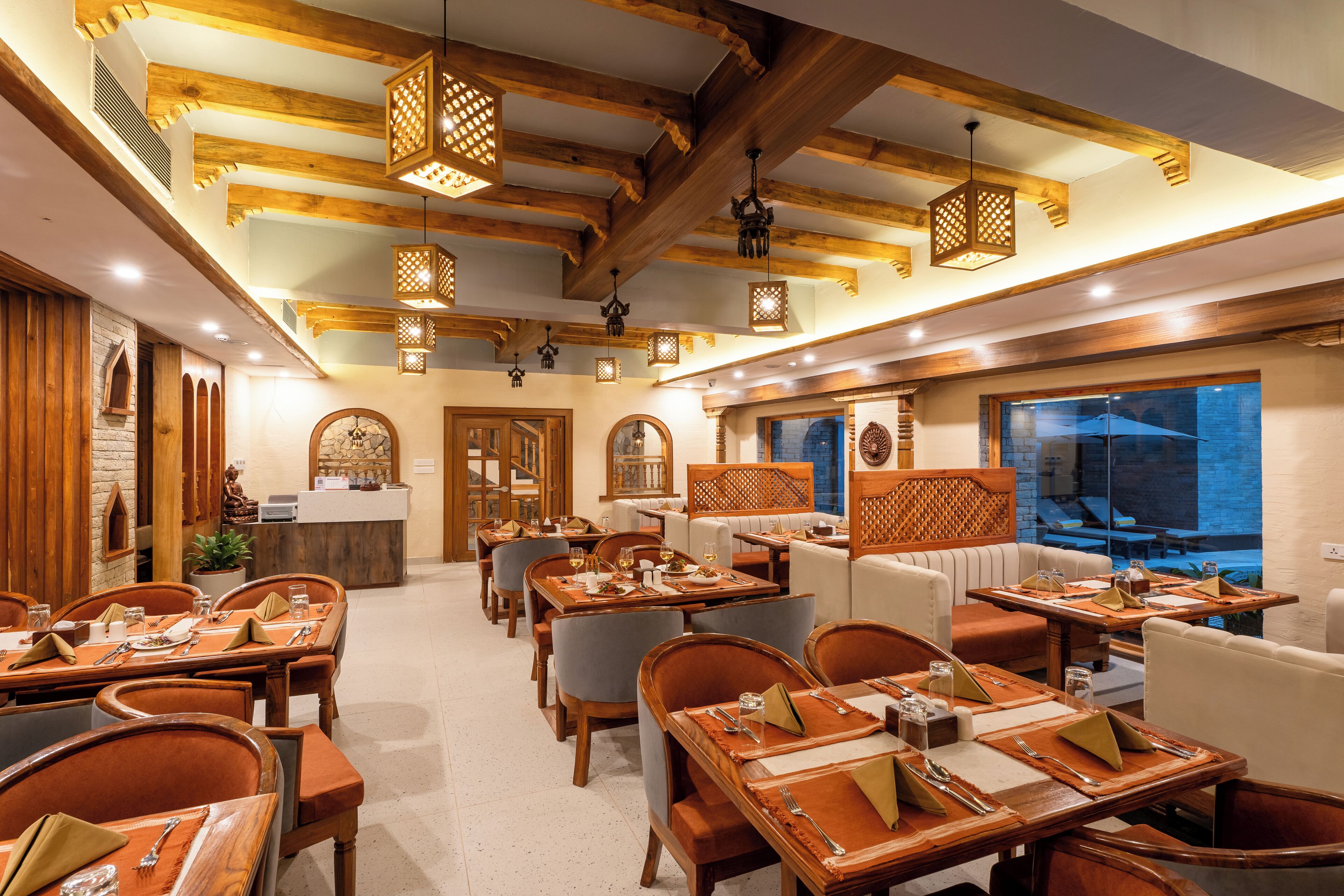 Ein Restaurant mit Holzbalken, hängenden Laternen und einer Mischung aus Holztischen und Polstermöbeln.