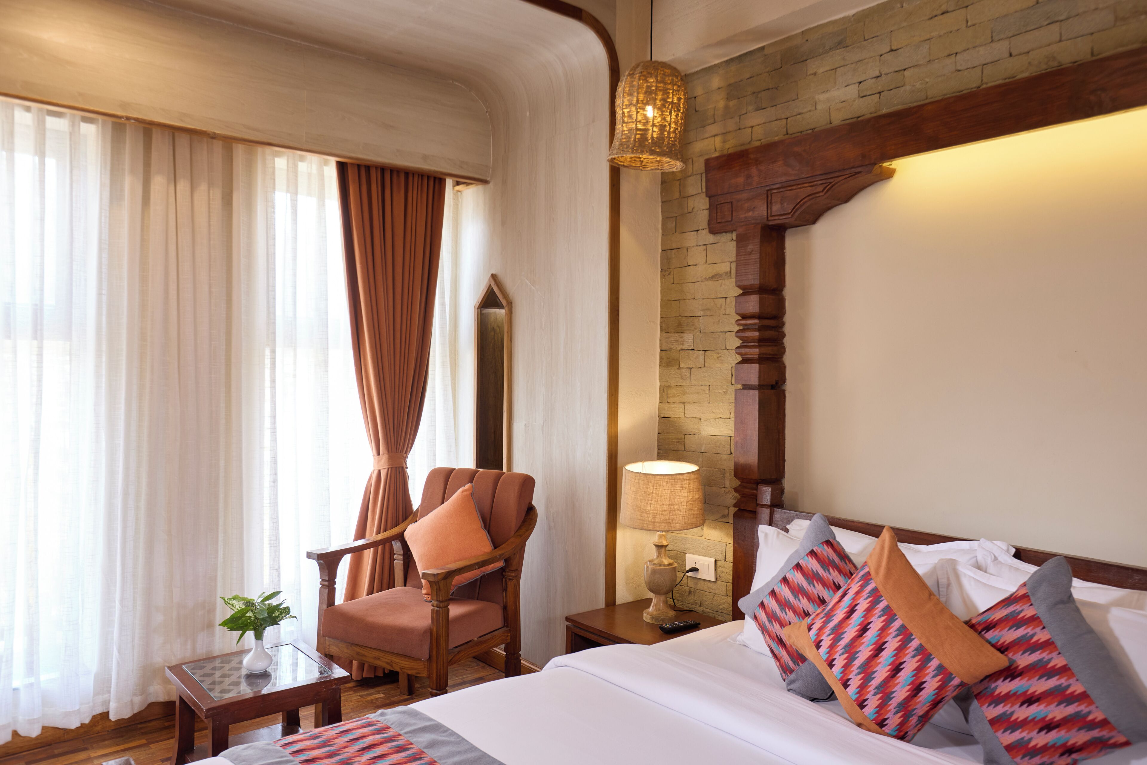 A hotel room with a bed, a chair, a lamp, a mirror, and a window with curtains.