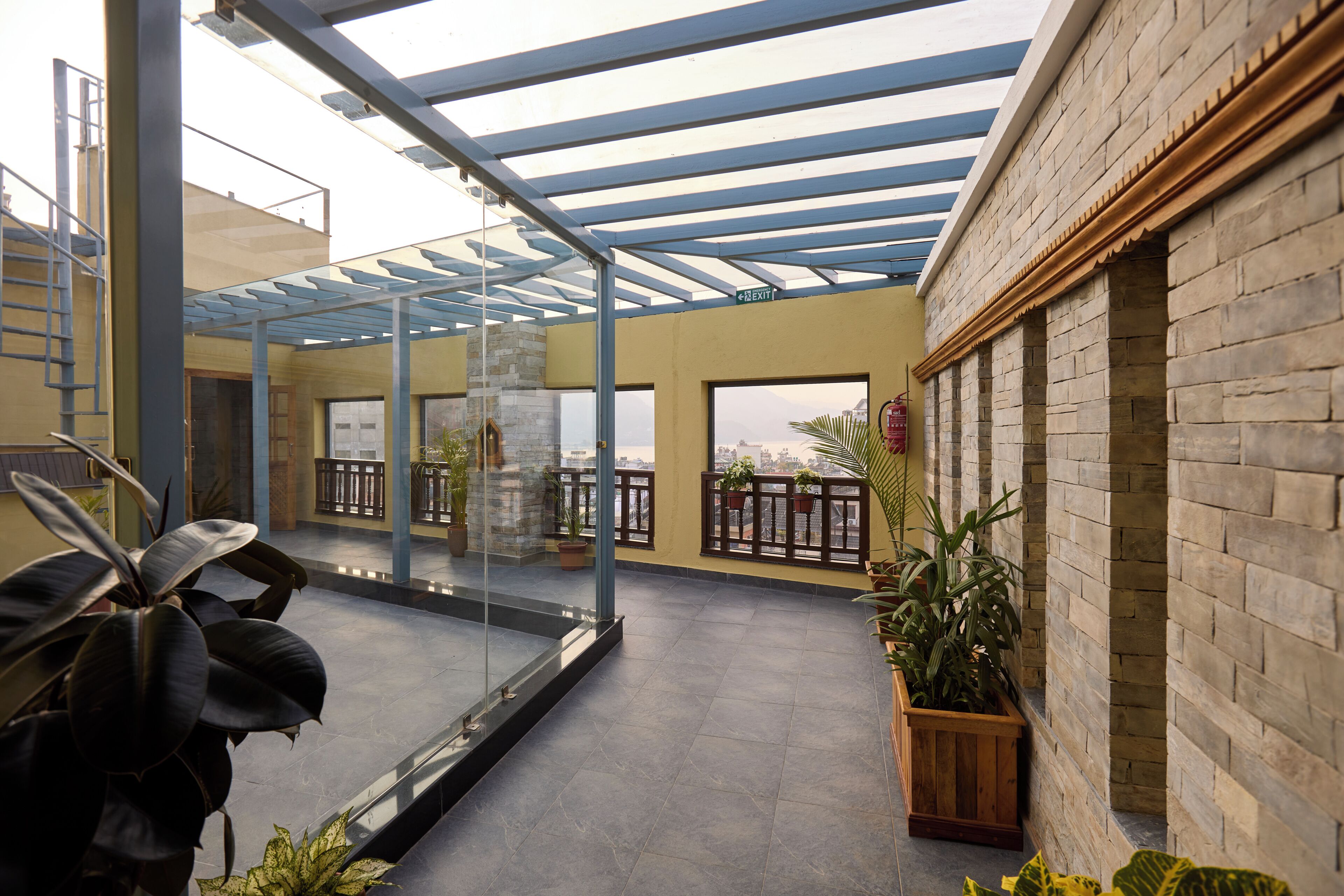 A covered outdoor area with a glass enclosure, potted plants, and a view of the city.