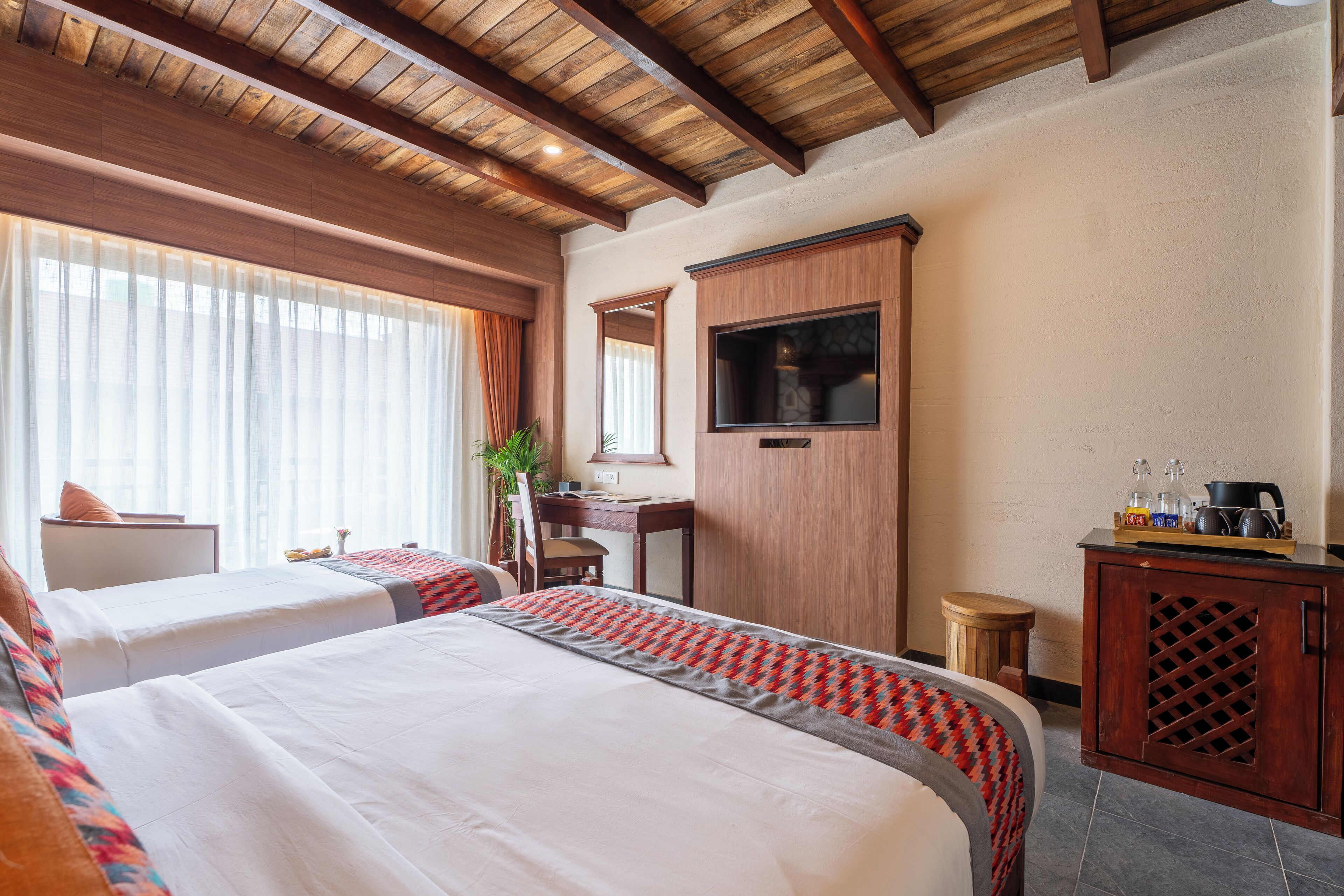 A hotel room with two beds, a wooden ceiling, a TV, a desk, and a cabinet.