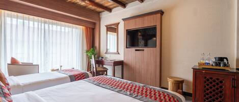 A hotel room with two beds, a wooden ceiling, a TV, a desk, and a cabinet.