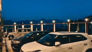 A parking area with several cars, a building with large windows, and mountains in the background. - The kempty fall resort (Dhanaulti)