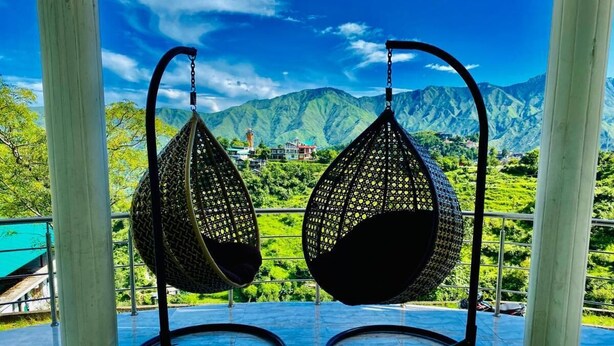 Two hanging chairs with a view of green mountains and a house in the background. - The kempty fall resort (Dhanaulti)