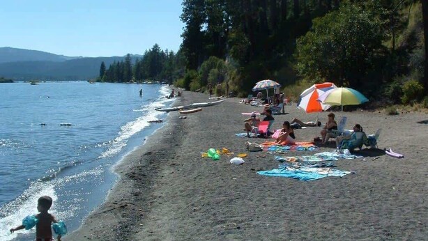 A beach with people relaxing under umbrellas, a child playing near the water, and boats in the background. - Walk to Beach & Ski, 4BR Custom Tahoe Home (Tahoe City)