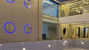 Una piscina interior moderna con paredes de azulejos azules, espejos circulares e iluminación contemporánea.