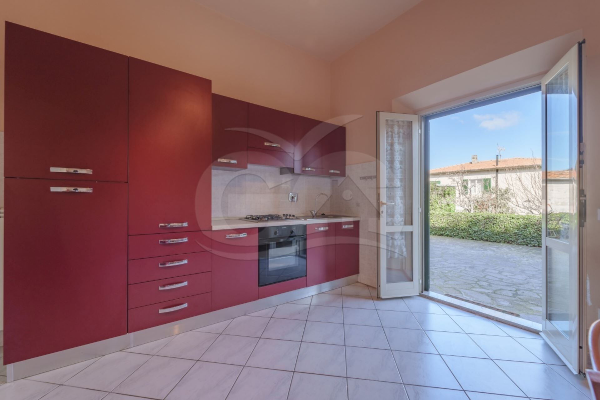 Una cocina moderna con armarios rojos, horno empotrado y un amplio ventanal corredero a un patio.