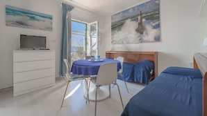 A room with a bed, a desk, a chair, a TV, and a window with a view of the sea.