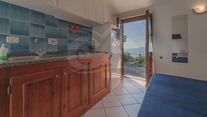 A kitchen with wooden cabinets, a granite countertop, and a view of the sea through an open door. - APPARTAMENTI NEREIDI - MONO NEREIDI (Capoliveri)