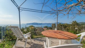 A patio with a round table and two chairs, overlooking a scenic view of the sea and hills. - APPARTAMENTI NEREIDI - MONO NEREIDI (Capoliveri)