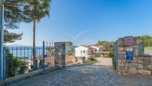 A stone pathway leading to a gated entrance with a view of houses and mountains in the background.