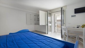 Ein Schlafzimmer mit Bett, Schreibtisch und Stuhl. Ein Kleiderschrank und ein Fernseher sind an der Wand angebracht.