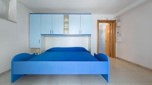 Ein Schlafzimmer mit einem Bett, weißen Wänden, einem blauen Kleiderschrank und einer Tür zu einem anderen Raum.
