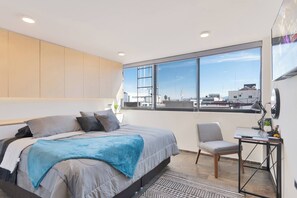 Un dormitorio moderno con una cama grande, un escritorio y vistas a la ciudad.