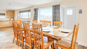 A dining area with a wooden table and chairs, a kitchen in the background, and a view through the window.