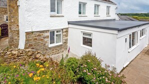A white house with stone walls, multiple windows, and a garden with flowers.